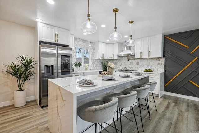 kitchen featuring a breakfast bar area, a kitchen island, white cabinets, stainless steel refrigerator with ice dispenser, and pendant lighting