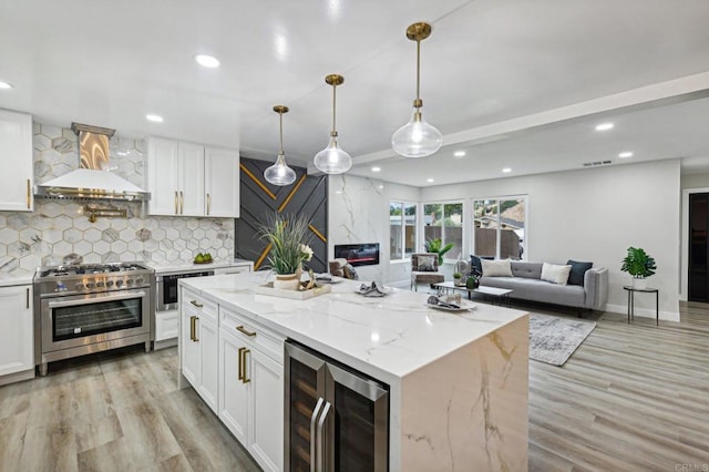 kitchen with stainless steel stove, white cabinetry, beverage cooler, and wall chimney exhaust hood