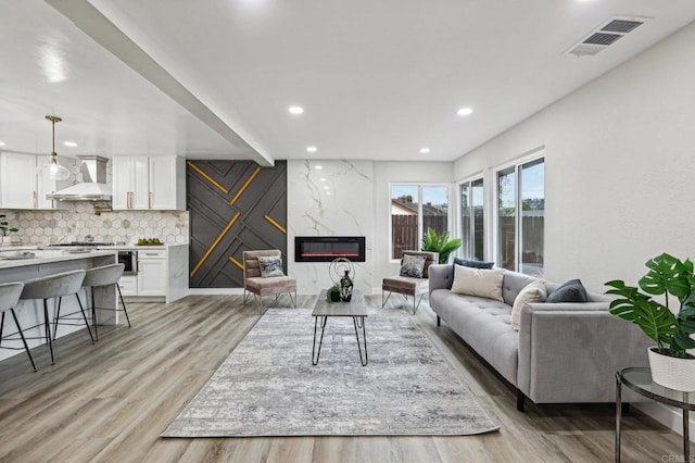 living room featuring light wood-style floors, recessed lighting, visible vents, and a high end fireplace