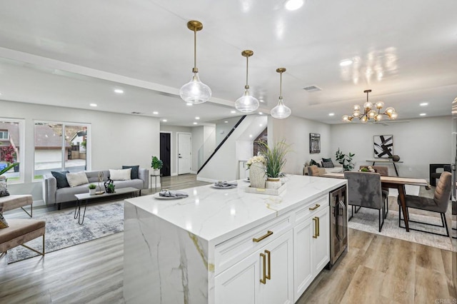 kitchen featuring hanging light fixtures, light stone counters, open floor plan, and white cabinets