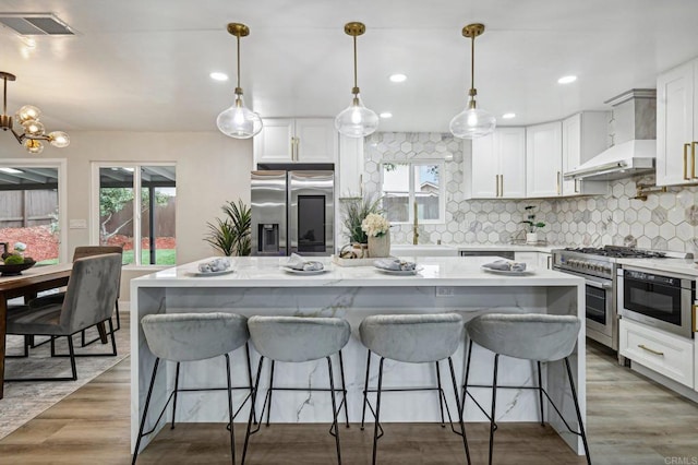 kitchen featuring wall chimney exhaust hood, appliances with stainless steel finishes, decorative light fixtures, and a center island