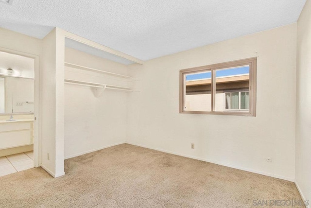 interior space featuring ensuite bathroom, sink, a textured ceiling, a closet, and light colored carpet