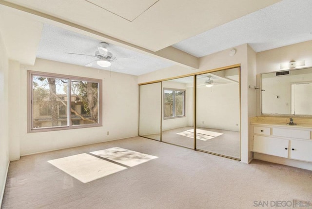 unfurnished bedroom with sink, ceiling fan, light carpet, a textured ceiling, and a closet