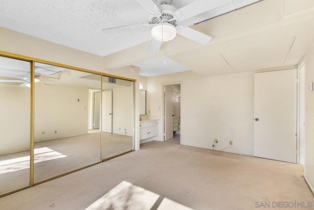 unfurnished bedroom with ensuite bathroom, light colored carpet, ceiling fan, and a textured ceiling