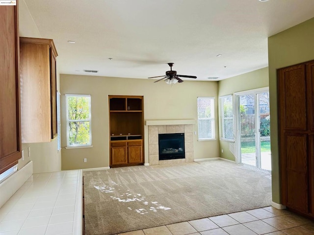 unfurnished living room featuring ceiling fan, a tiled fireplace, and light carpet