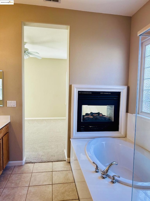 bathroom with tile patterned floors, a multi sided fireplace, vanity, tiled tub, and ceiling fan