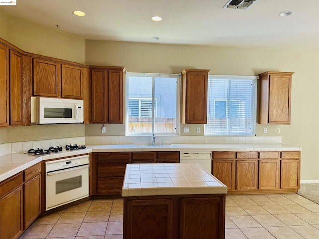 kitchen with tile countertops, sink, a center island, light tile patterned floors, and white appliances