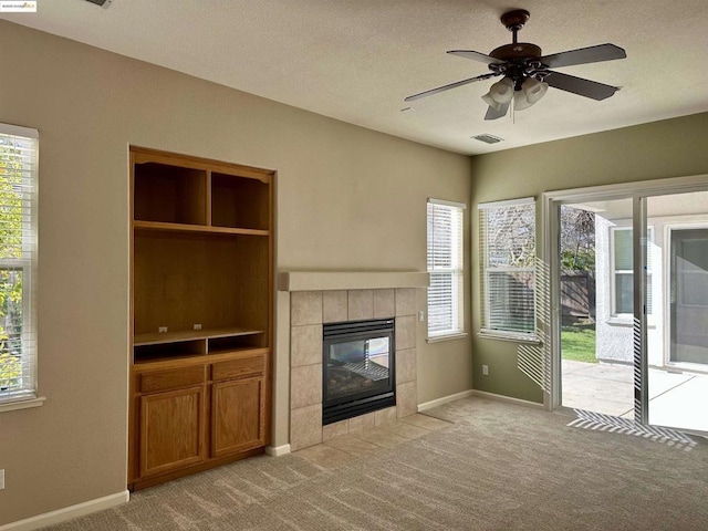 unfurnished living room with a tile fireplace, light carpet, a textured ceiling, and ceiling fan