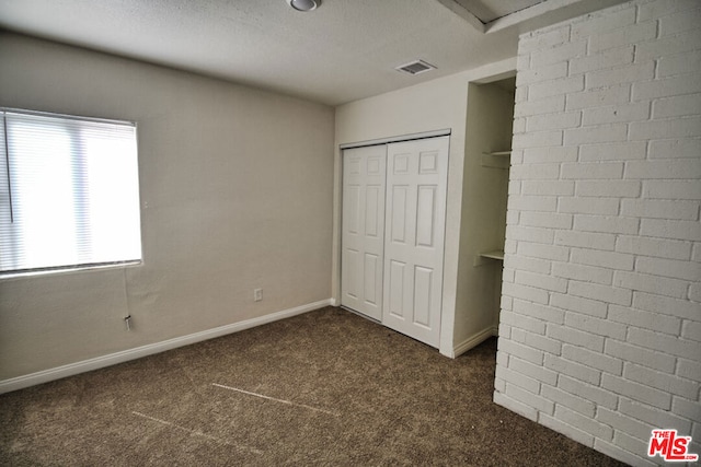 unfurnished bedroom with a closet, a textured ceiling, and dark colored carpet