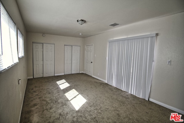 unfurnished bedroom featuring multiple closets and dark colored carpet