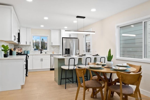 kitchen with appliances with stainless steel finishes, a kitchen island, white cabinetry, decorative backsplash, and hanging light fixtures