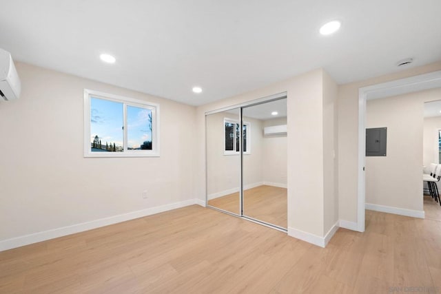 unfurnished bedroom featuring a closet, electric panel, light hardwood / wood-style floors, and a wall unit AC