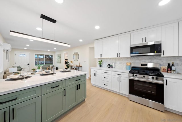 kitchen featuring green cabinets, hanging light fixtures, stainless steel appliances, light hardwood / wood-style floors, and white cabinets