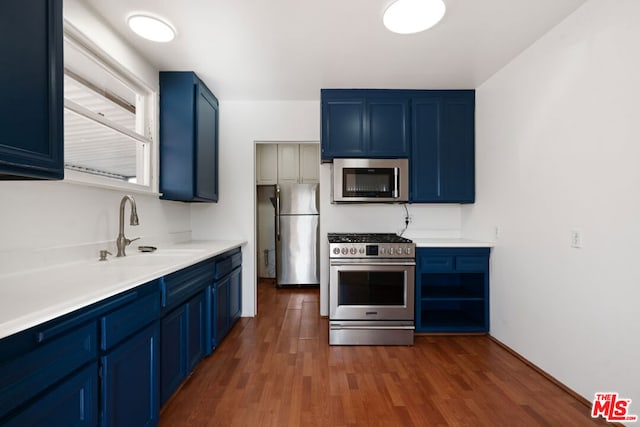 kitchen with blue cabinets, appliances with stainless steel finishes, sink, and dark hardwood / wood-style floors