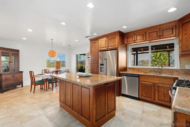 kitchen featuring pendant lighting, sink, appliances with stainless steel finishes, a center island, and light stone counters