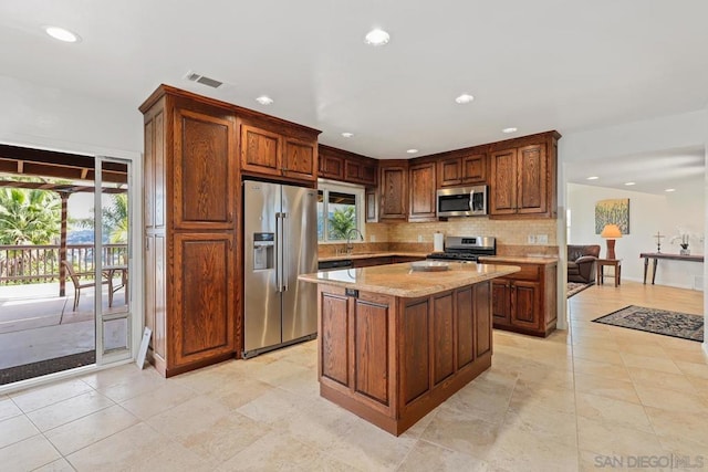 kitchen featuring sink, tasteful backsplash, light stone counters, a kitchen island, and stainless steel appliances