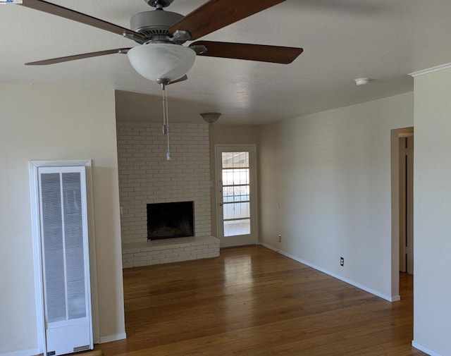 unfurnished living room featuring a brick fireplace, dark wood-type flooring, and ceiling fan