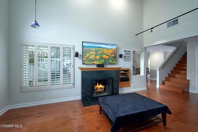 living room featuring a premium fireplace, wood-type flooring, and a towering ceiling