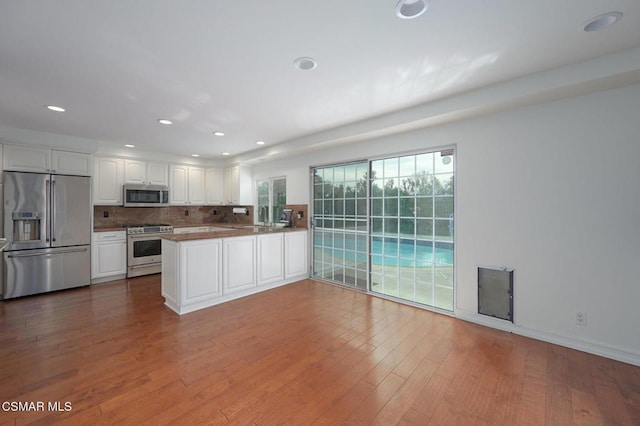 kitchen with white cabinetry, stainless steel appliances, tasteful backsplash, wood-type flooring, and kitchen peninsula