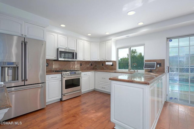 kitchen featuring light hardwood / wood-style flooring, stainless steel appliances, kitchen peninsula, and white cabinets