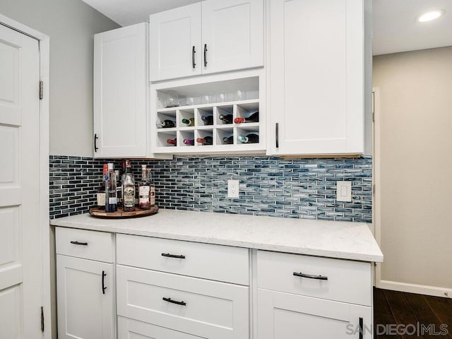 bar featuring light stone counters, backsplash, dark hardwood / wood-style flooring, and white cabinets