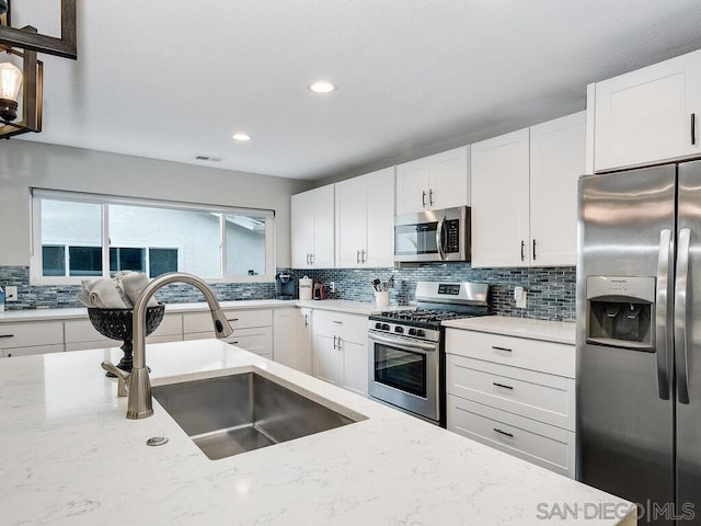 kitchen with tasteful backsplash, white cabinetry, sink, stainless steel appliances, and light stone countertops