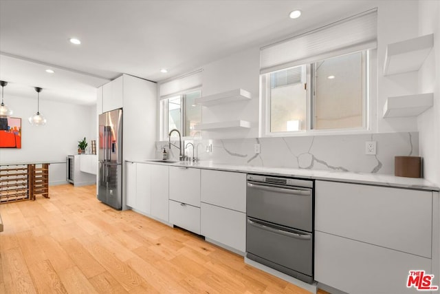 kitchen with a wealth of natural light, decorative light fixtures, white cabinetry, sink, and high end fridge