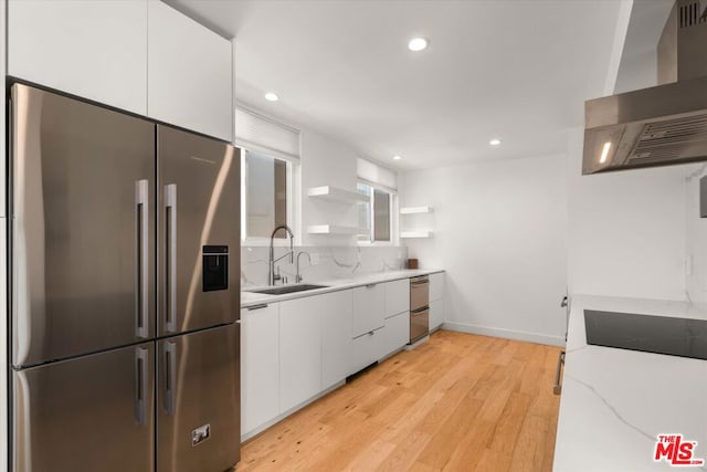 kitchen featuring wall chimney exhaust hood, sink, stainless steel appliances, light stone countertops, and white cabinets