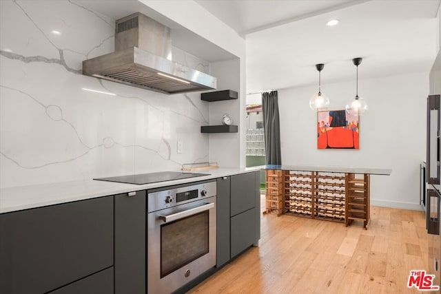 kitchen with stainless steel oven, ventilation hood, hanging light fixtures, black electric stovetop, and light hardwood / wood-style floors