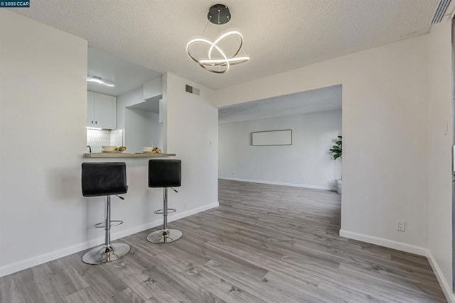 kitchen featuring white cabinetry, a breakfast bar area, backsplash, kitchen peninsula, and light wood-type flooring