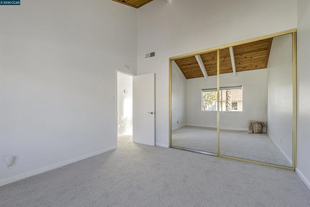 unfurnished bedroom featuring wood ceiling, beam ceiling, high vaulted ceiling, carpet flooring, and a closet