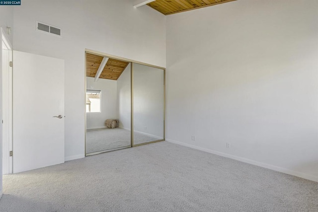 unfurnished bedroom with high vaulted ceiling, wooden ceiling, a closet, beam ceiling, and carpet