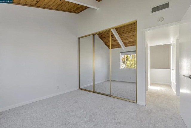 unfurnished bedroom featuring light colored carpet, lofted ceiling with beams, wooden ceiling, and a closet