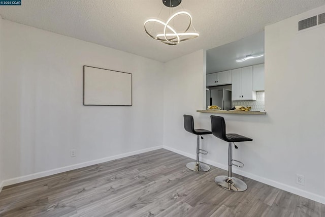 unfurnished dining area with a notable chandelier, light hardwood / wood-style floors, and a textured ceiling