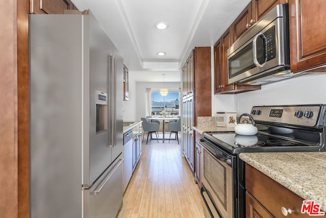 kitchen featuring stainless steel appliances, light stone countertops, pendant lighting, and light wood-type flooring