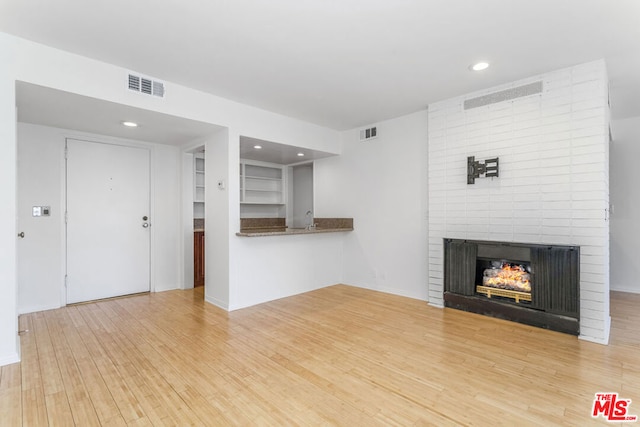 unfurnished living room featuring a multi sided fireplace and light wood-type flooring