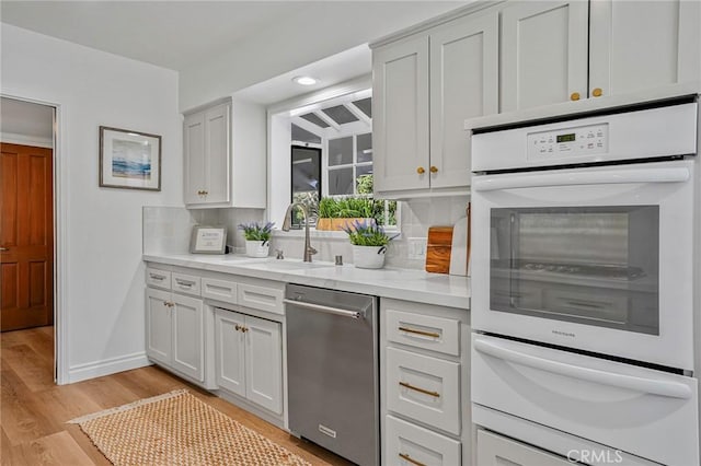 kitchen with sink, white double oven, dishwasher, backsplash, and light wood-type flooring