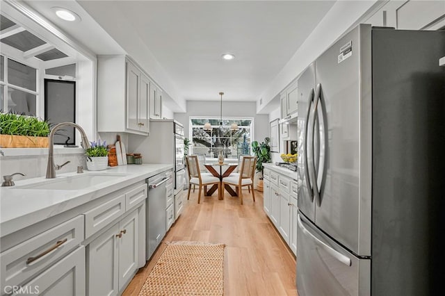 kitchen featuring appliances with stainless steel finishes, decorative light fixtures, sink, light stone countertops, and light wood-type flooring