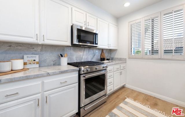 kitchen featuring white cabinetry, stainless steel appliances, light stone countertops, decorative backsplash, and light wood-type flooring