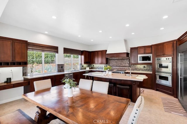 kitchen featuring appliances with stainless steel finishes, backsplash, a kitchen breakfast bar, custom range hood, and a center island with sink