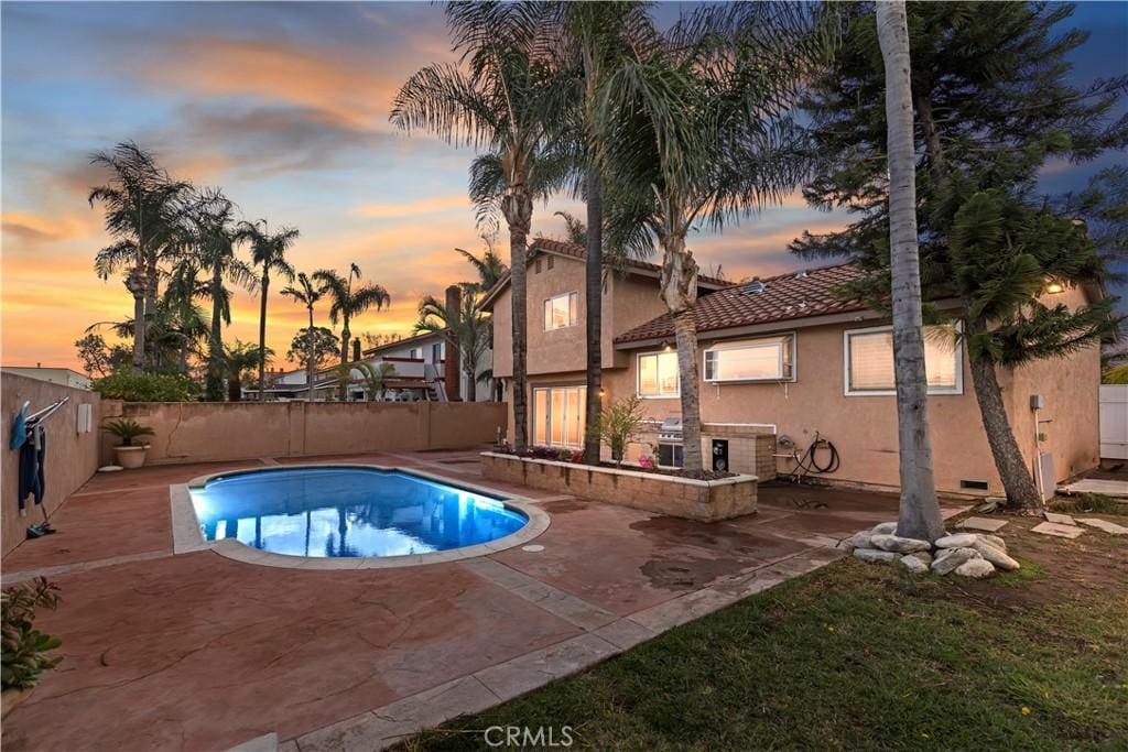 pool at dusk featuring grilling area and a patio area