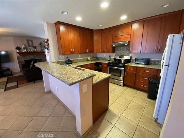 kitchen with light tile patterned floors, stainless steel range with gas stovetop, light stone countertops, kitchen peninsula, and white fridge