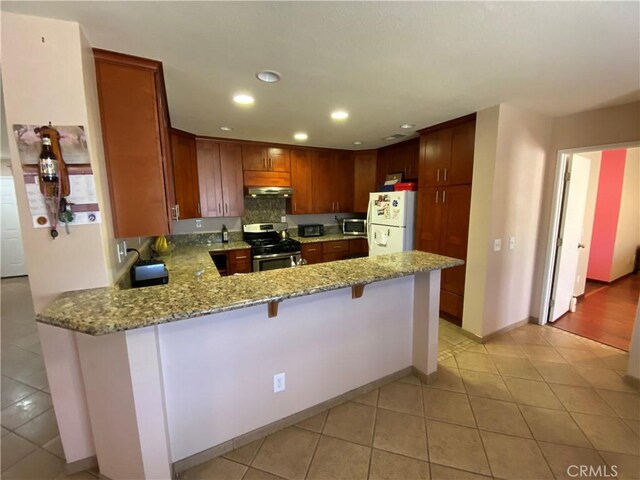 kitchen featuring light stone counters, appliances with stainless steel finishes, kitchen peninsula, and a breakfast bar area