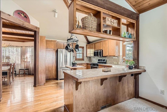 kitchen featuring appliances with stainless steel finishes, vaulted ceiling with beams, tile counters, decorative backsplash, and kitchen peninsula