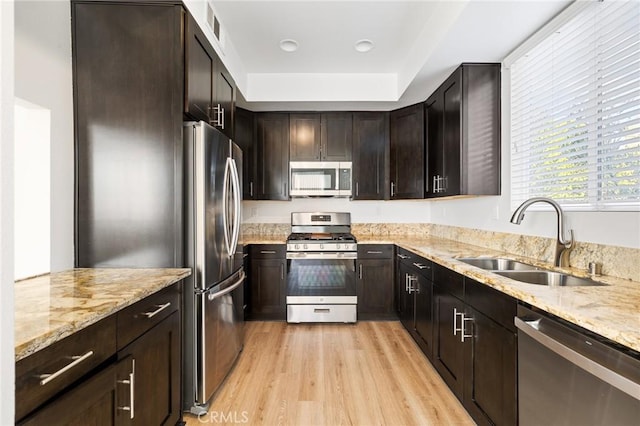 kitchen featuring sink, stainless steel appliances, dark brown cabinetry, light hardwood / wood-style floors, and light stone countertops