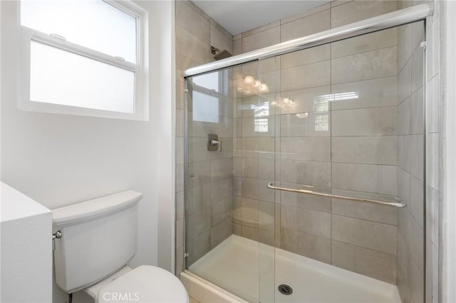 bathroom featuring a shower with door and toilet