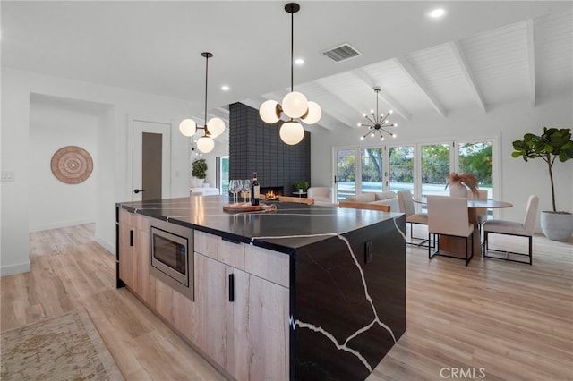 kitchen featuring pendant lighting, vaulted ceiling with beams, a center island, stainless steel microwave, and light hardwood / wood-style floors