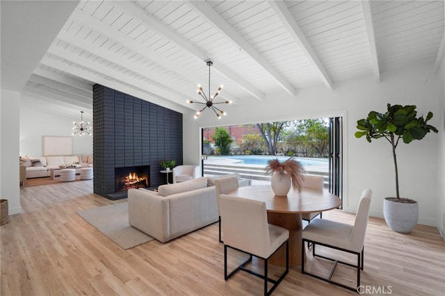 interior space with an inviting chandelier, a brick fireplace, light hardwood / wood-style flooring, and vaulted ceiling with beams