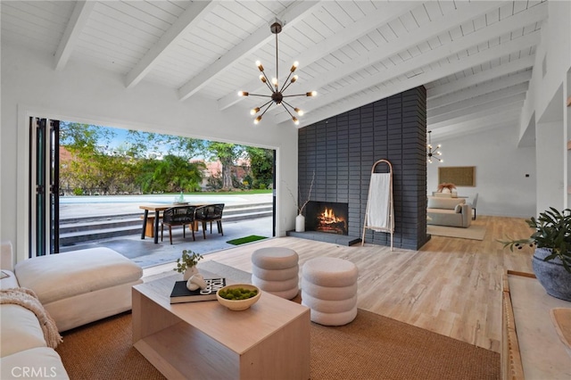 living room with an inviting chandelier, wood-type flooring, a brick fireplace, and vaulted ceiling with beams