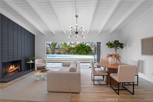 living room featuring a brick fireplace, beam ceiling, light hardwood / wood-style flooring, and a chandelier